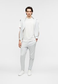 Αθλητική εμφάνιση σε ανοιχτό γκρι χρώμα που περιλαμβάνει κοντομάνικο πουκάμισο και στενά παντελόνια, κατασκευασμένα από λείο ύφασμα, με casual σχεδίαση και ελάχιστο λογότυπο.