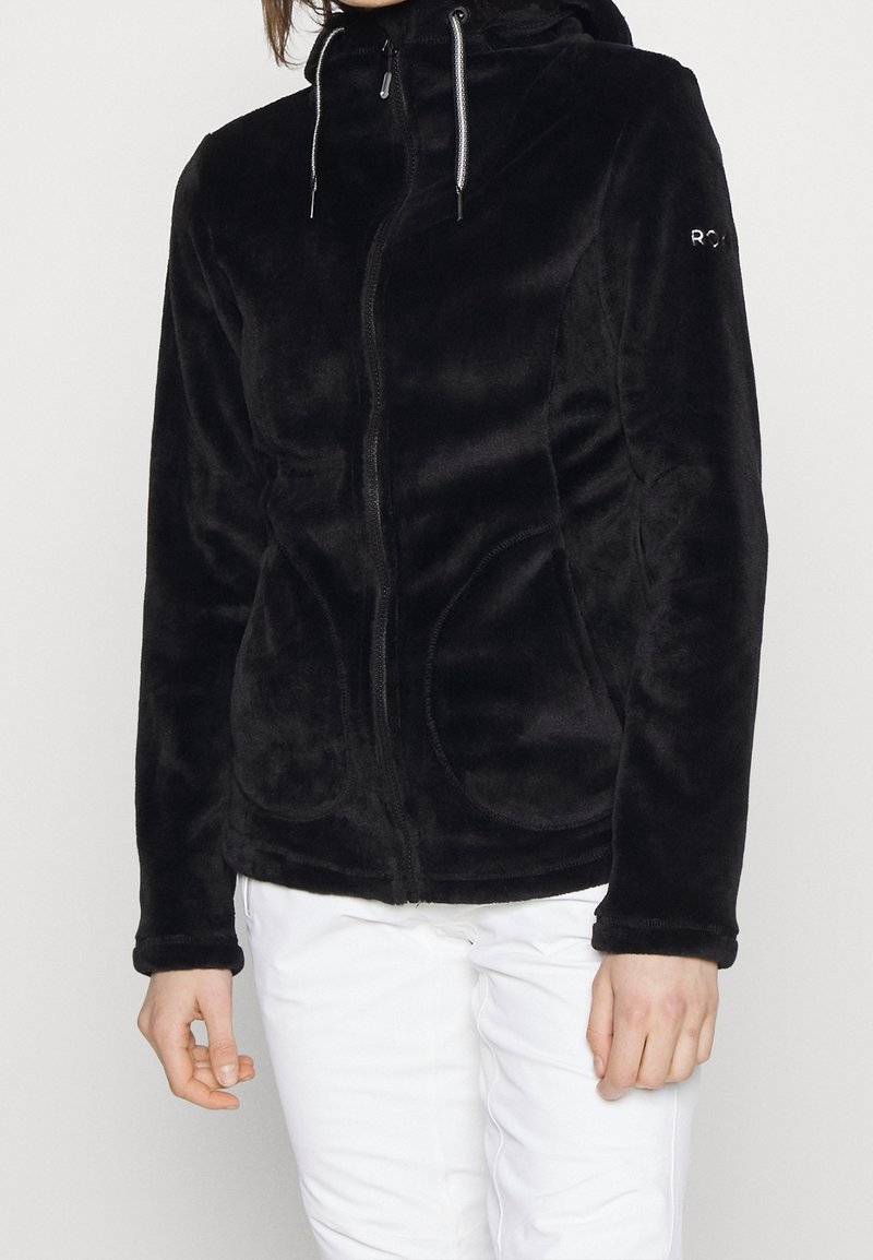 Black fleece jacket with a zippered front, adjustable hood, side pockets, and smooth texture. Features contrasting stitching and logo on sleeve.