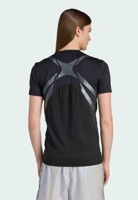 Zwarte sportieve t-shirt met reflecterende zilveren accenten en een uniek ontwerp op de achterkant, gecombineerd met lichtgrijze shorts.
