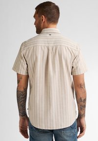 Camisa beige de manga corta con finas rayas verticales, diseño casual, pliegue en la espalda y dobladillo redondeado, combinada con jeans azul oscuro.
