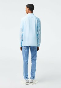 Camicia azzurra a maniche lunghe con colletto button-down, abbinata a jeans azzurri e sneakers bianche. Tessuto morbido con vestibilità rilassata.