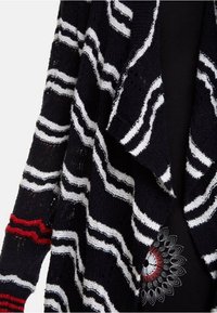 Cardigan a righe bianche e nere in materiale lavorato a maglia, con un design morbido, apertura frontale e dettagli rossi sulle maniche.