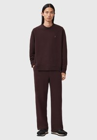 Sweatshirt castanho e calças combinando em um tecido liso e suave. Corte descontraído com punhos canelados; apresenta um pequeno logotipo no peito.