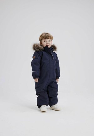 Marineblå børnesnowsuit med pelsforet hætte, elastiske manchetter, fuld lynlås og et lille brunt logo-patch på ærmet. Letvægtsstof.