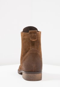 Hnědé semišové kotníkové boty s kulatou špičkou, švy a dřevěným podpatkem. Na zadní straně se nachází malá poutko pro snadnější obutí.