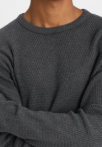 Pull gris foncé texturé avec un col large et des manches longues, arborant un motif gaufré pour plus de détail et de chaleur.