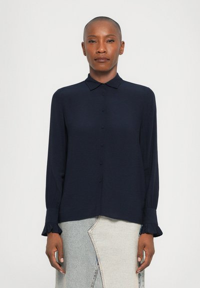 Chemise bleu marine à boutons, fabriquée en tissu lisse, dotée d'un col et de poignets volantés, associée à une jupe en denim clair avec des détails de couture.