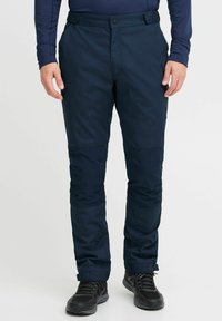Pantaloni tehnici bleumarin cu închidere prin buton, buzunare laterale, panouri întărite la genunchi și tivuri ajustabile, asortați cu pantofi sport negri.