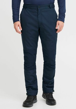 Pantalones técnicos azul marino con cierre de botón, bolsillos laterales, paneles de rodilla reforzados y puños ajustables, combinados con zapatillas deportivas negras.