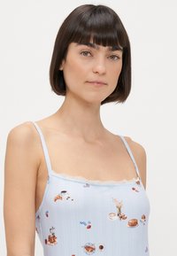 Jasnoniebieska koszulka na ramiączkach z regulowanymi paskami, zdobiona koronkowym wykończeniem i wzorem z ilustracjami jedzenia, w tym wypieków i napojów.