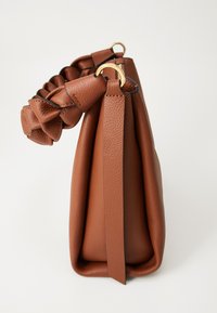 Brown leather handbag with gathered, ruffled top handle and gold metal rings, shown from a side angle on a white background.