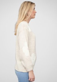 Helles beiges Sweatshirt mit weißen Blumenmustern, gestrickter Textur, Rundhalsausschnitt und lockerer Passform. Lange Ärmel und gerippte Bündchen runden das Design ab.