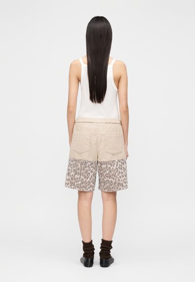 Μπεζ σορτς με λεοπάρ τύπωμα στο κάτω μέρος, διαθέτουν ελαστική μέση, δύο πίσω τσέπες και φοριούνται με σκουρόχρωμες πλεκτές κάλτσες.