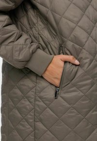 Quilted grå jakke med lynlåslommer, ribbede manchetter og en glat, skinnende tekstur. Jakken har et slankt, tætsiddende design.