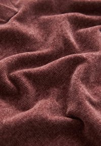 Soft, textured fabric in a deep mauve color, arranged in folds, showcasing its plush surface and subtle sheen.