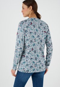 Camisa de manga larga en gris claro con estampados florales en verde azulado, burdeos y verde. Tejido suave con un corte relajado y escote redondo.