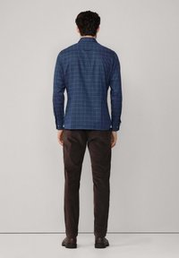 Blauw geruit shirt met lange mouwen, knopenmanchetten en een naar beneden vallende kraag; gecombineerd met donkerbruine broeken en laarzen.