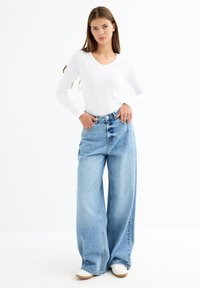 Blusa blanca de manga larga ligera con cuello redondo, combinada con unos vaqueros de mezclilla azul claro de tiro alto y con botón, de corte oversize.