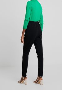 Zwarte taps toelopende broek met een elastische tailleband, gecombineerd met een felgroen aansluitend topje en beige sandalen met banden. Glad materiaal, minimaal ontwerp.
