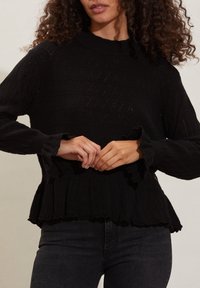 Pull en tricot noir avec un motif en diamant texturé, des manches volantes et un ourlet peplum. Comprend des accents côtelés au niveau des poignets.