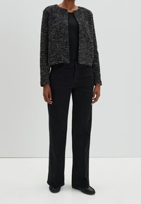 Veste courte noire à texture, à encolure ronde, associée à un pantalon noir taille haute, offrant une coupe décontractée avec une légère évasée.