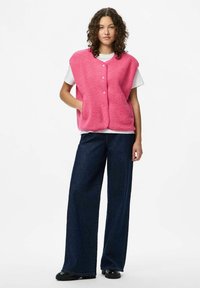 Rosa fleeceväst med knäppning framtill, två fickor och en avslappnad passform, parat med vida, mörka denimbyxor och svarta skor.