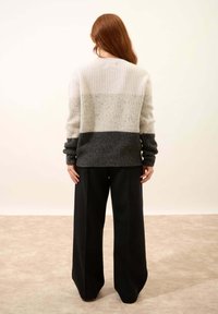 Sweter dziany z gradientowym wzorem; jasnoszara góra, nakrapiana środkowa część i ciemnoszara dolna. Połączony z czarnymi spodniami o szerokich nogawkach.