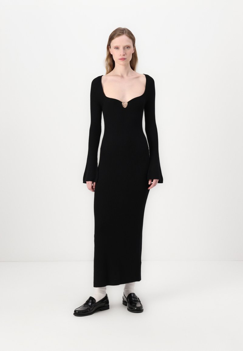 Abito nero in maglia con scollatura profonda, maniche lunghe e polsini a campana. Presenta un accento decorativo dorato sul petto.