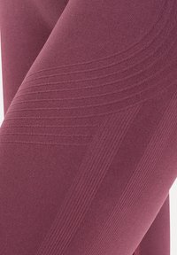 Gros plan d’un tissu texturé, côtelé, couleur rose poussière avec des motifs de tricot courbes et linéaires créant un détail de design tactile et structuré.