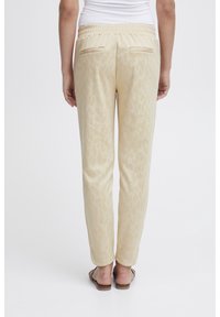 Beżowe spodnie dresowe z subtelnym zwierzęcym wzorem, elastycznym paskiem w talii i dwiema tylnymi kieszeniami. Miękki materiał o gładkiej teksturze.