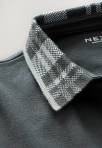Grå polo shirt med en tekstureret ternet krave i grå og hvid. Blødt stof med en glat overflade og knapdetalje.