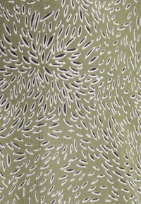 Tissu vert avec un motif répétitif de formes allongées blanches et noires, créant un design texturé et organique.