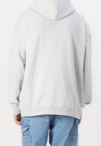 Szara bluza z kapturem wykonana z miękkiego materiału, o luźnym kroju, z prążkowanymi mankietami i dolnym brzegiem, o gładkim designie. Widoczna kieszeń na dłonie.