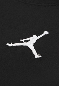 Czarna tkanina z białym haftowanym konturem skaczącej postaci trzymającej piłkę do koszykówki, z szczegółowym przeszyciem i teksturą.