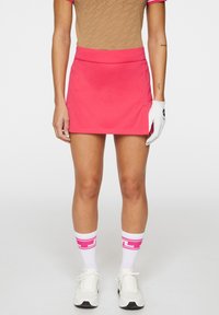 Roze golfrok met een strakke tailleband. Draagt een gepatroneerde beige top, witte sokken met roze strepen en witte sportschoenen.