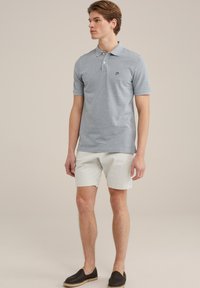 Pelēks īsām piedurknēm polo krekls ar apkakli un mazu logotipu uz krūšu, apvienots ar gaišiem šortiem un melnām slip-on kurpēm.