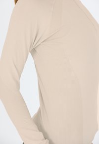 Beige langærmet top med ribbet tekstur, tætsiddende design, sømløs konstruktion og teksturerede detaljer på ærmerne.