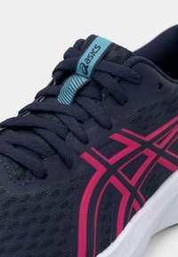 Chaussure de running ASICS bleu marine avec bandes de logo roses, étiquette de languette bleue marquée et lacets épais bleu marine sur semelle blanche.
