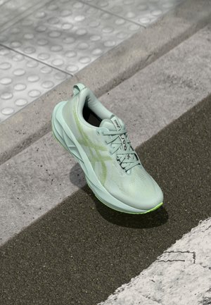 Scarpa da corsa verde chiaro con tomaia testurizzata, lacci e dettagli riflettenti. Presenta un intersuola ammortizzata e una suola in gomma per una maggiore trazione.