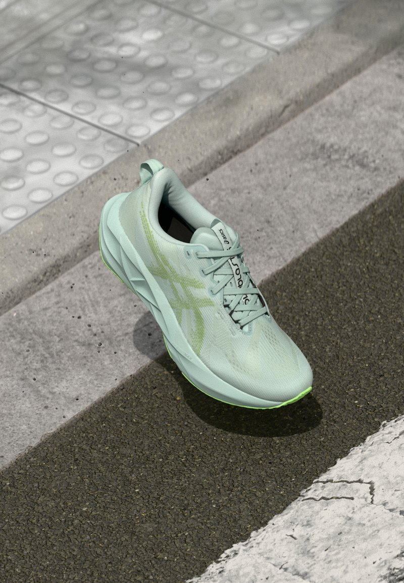 Scarpa da corsa verde chiaro con tomaia testurizzata, lacci e dettagli riflettenti. Presenta un intersuola ammortizzata e una suola in gomma per una maggiore trazione.