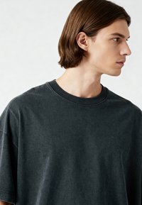 Tamsiai pilkas, per didelis marškinėliai, pagaminti iš minkštos medvilnės. Yra apvalus kaklas, trumpomis rankovėmis ir šiek tiek nusidėvėjęs tekstūros. Paprastas dizainas.