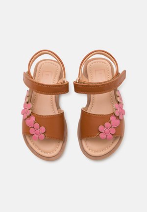 Sandales marron pour enfants avec décorations roses en forme de fleurs et de cœurs et brides auto-agrippantes à la cheville sur fond blanc.