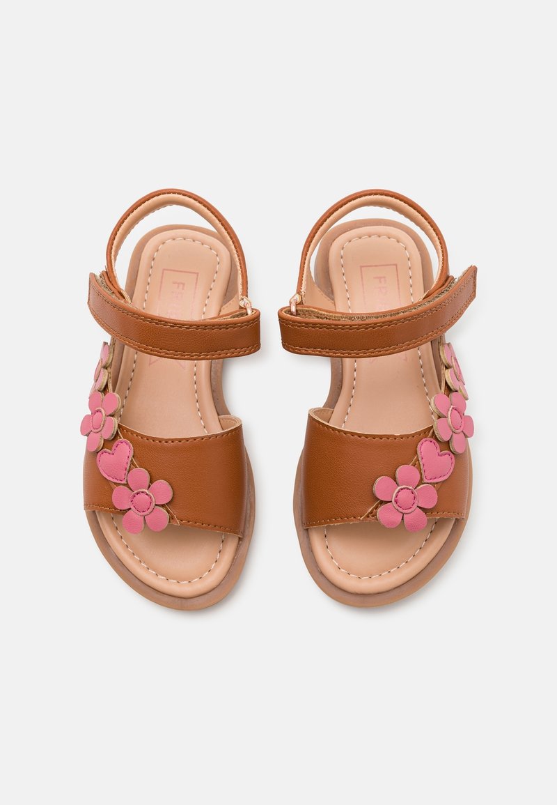 Sandales marron pour enfants avec décorations roses en forme de fleurs et de cœurs et brides auto-agrippantes à la cheville sur fond blanc.