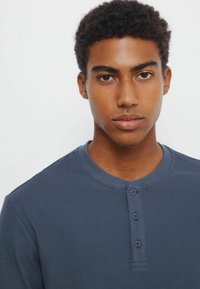 Navyblaues Langarm-Henley-Shirt aus strukturiertem Stoff, mit Rundhalsausschnitt und einer Knopfleiste mit drei Knöpfen.