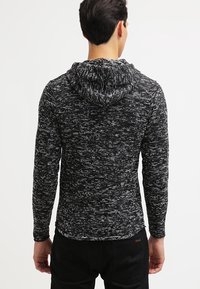 Felpa con cappuccio a maglia maculata bianca e nera con finitura testurizzata, maniche lunghe e cappuccio con cordino, abbinata a pantaloni neri.