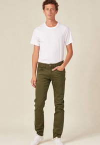 Pantalones verdes ajustados de algodón con una textura suave, combinados con una camiseta básica blanca de cuello redondo y zapatillas blancas.