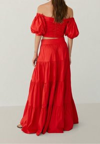 Ensemble rouge deux pièces comprenant un haut court à épaules dénudées avec des manches bouffantes et une jupe longue à volants, tous deux en tissu léger.