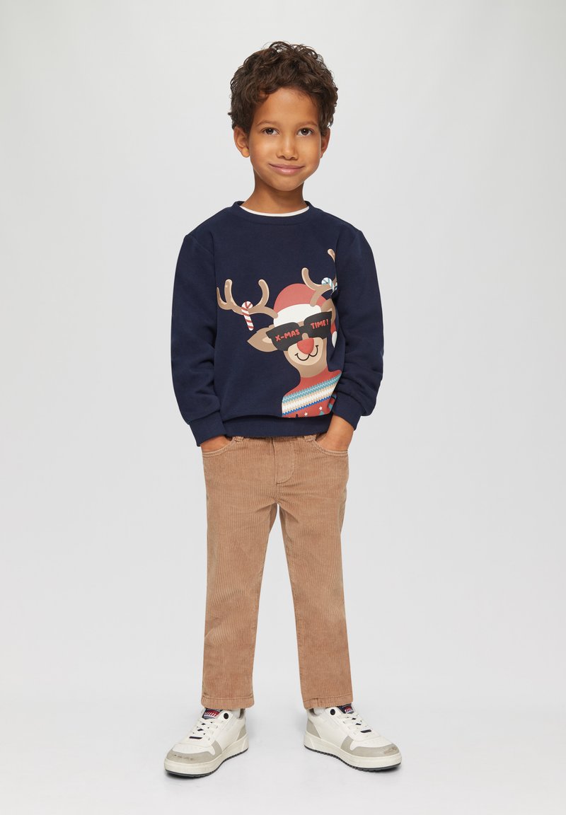 Marineblauer Sweatshirt mit einem Rentiermotiv und Text, kombiniert mit beigen Cordhosen und weißen Sneakers. Lässiges Outfit für Kinder.