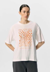 Camiseta de algodón blanca con un gráfico floral naranja que incluye el texto "LIBERA TU MENTE" y "LO DEMÁS SE SEGUIRÁ". Corte cuadrado y mangas cortas.