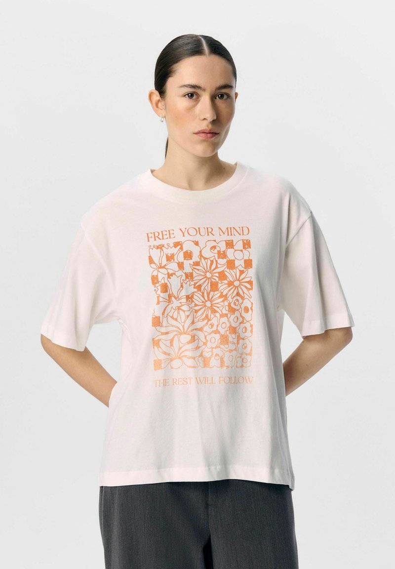 Camiseta de algodón blanca con un gráfico floral naranja que incluye el texto "LIBERA TU MENTE" y "LO DEMÁS SE SEGUIRÁ". Corte cuadrado y mangas cortas.